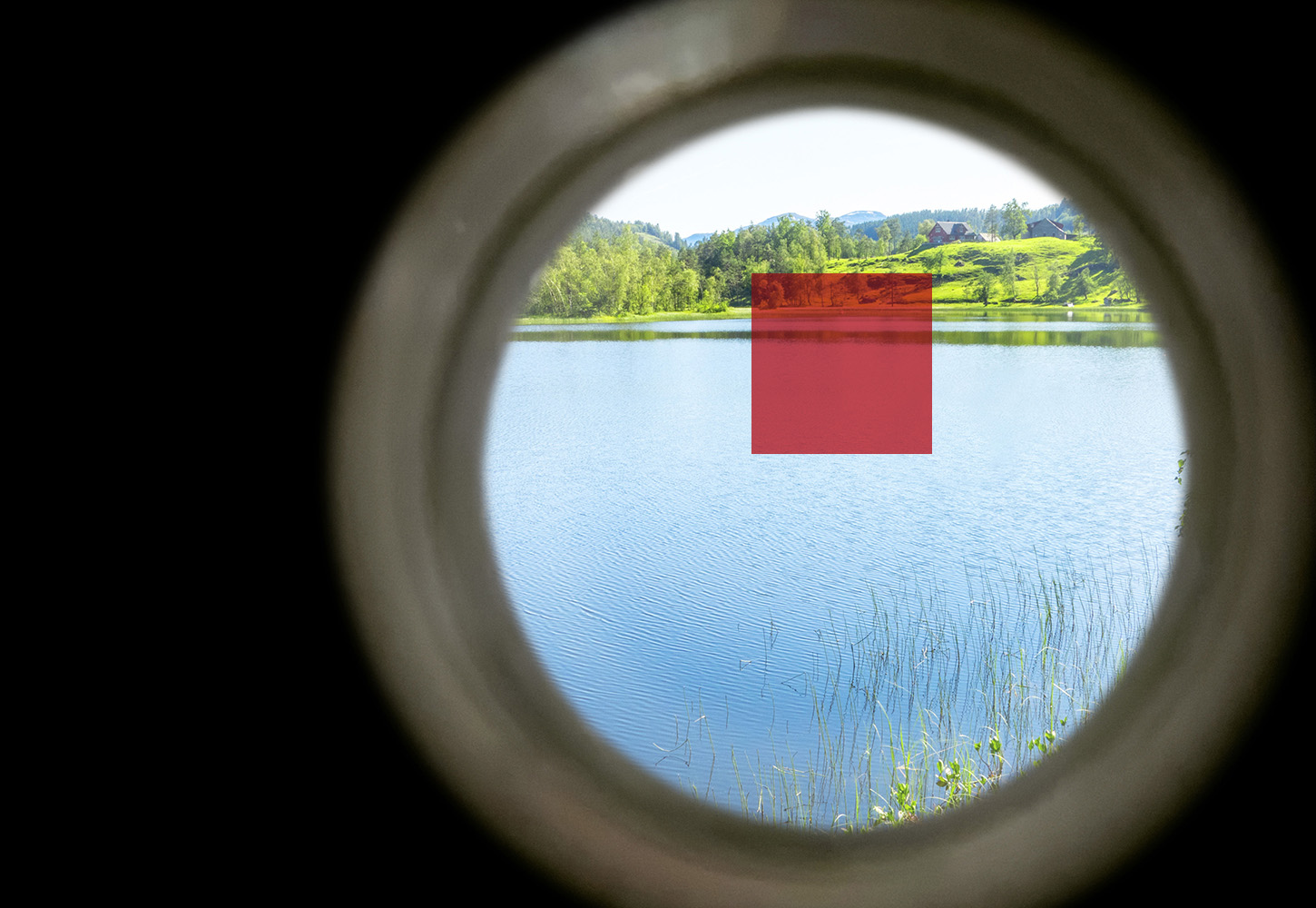 Blick durch ein Rohr auf einen See mit Schilf und Bergen